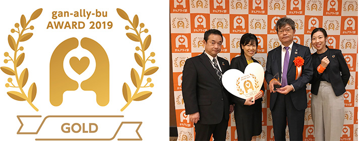 日立システムズが受賞した「がんアライアワード2019 GOLD」ロゴ(左)、「がんアライアワード 2019」表彰式の様子(右)