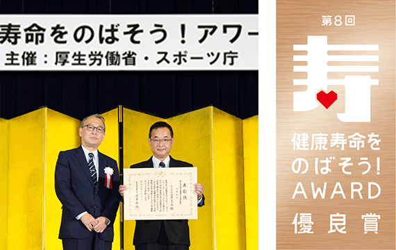 表彰式の様子（左）と「健康寿命をのばそう！アワード」のロゴマーク（右）。写真は左側が厚生労働省 健康局 局長 宮嵜 雅則氏、右側が日立システムズ 人事総務本部 安全衛生管理センタ センタ長 今村 隆（右）